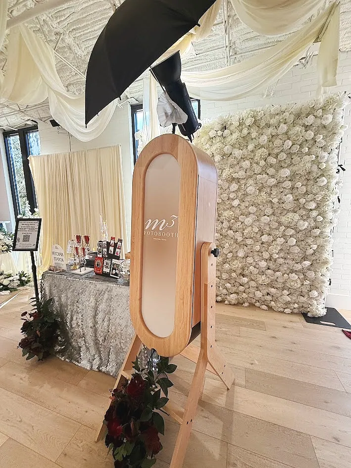 The wood framed Dreamy Luxe mirror booth beside a white flower wall