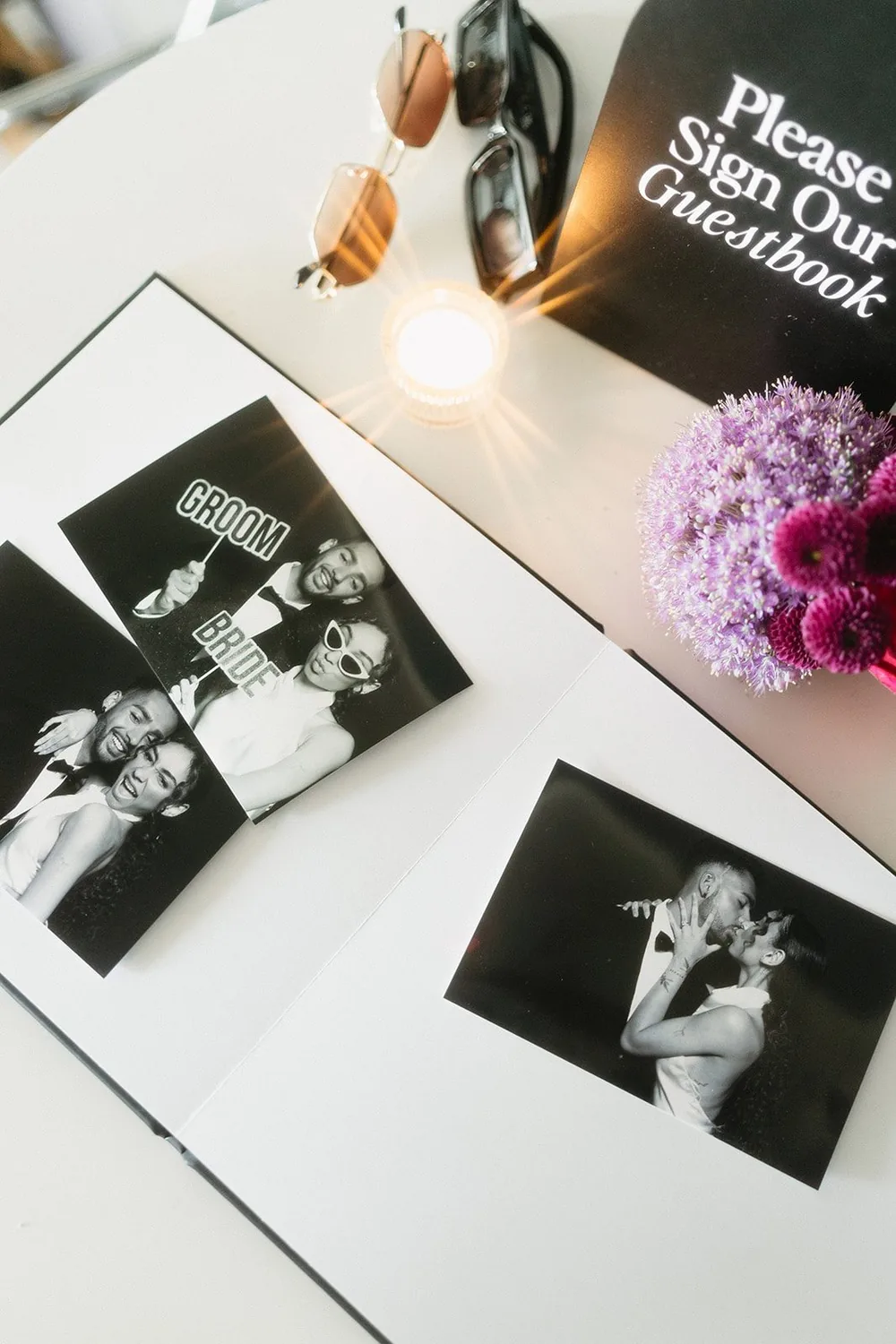 An open photo guest book with booth prints on its pages, beside a sign asking guests to sign it