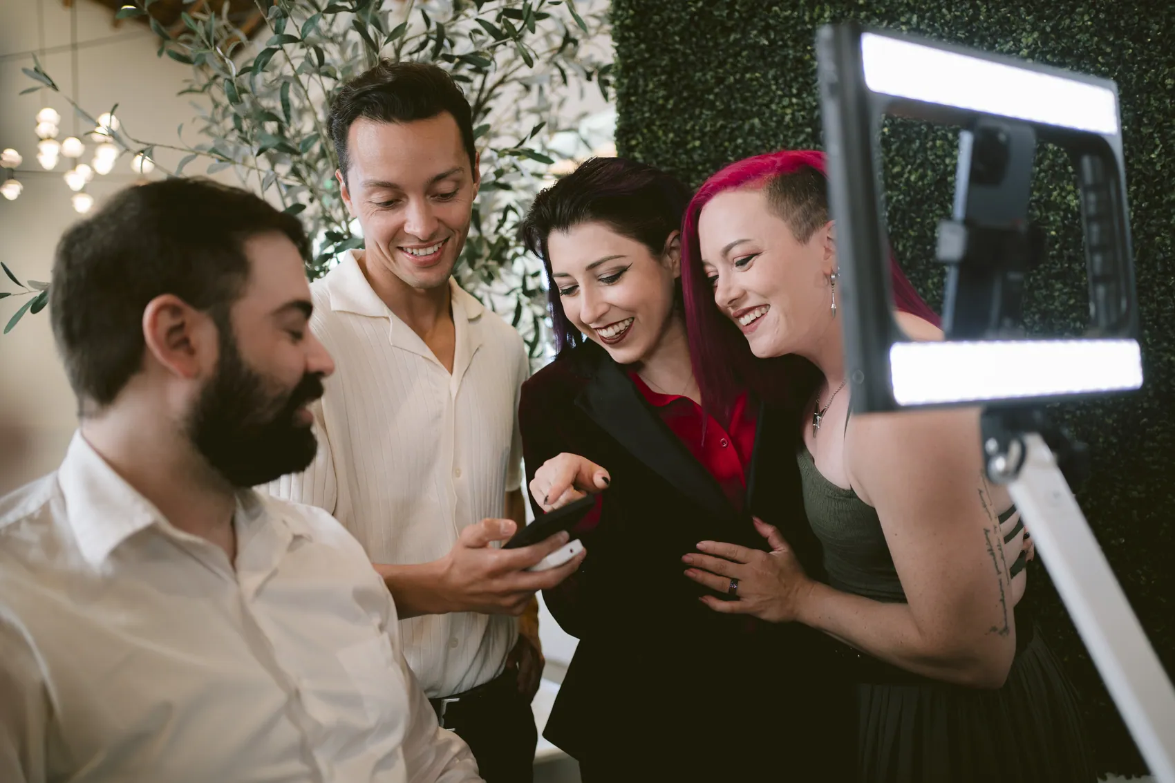 Four guests leaning in together over a phone, looking at the photo they just took