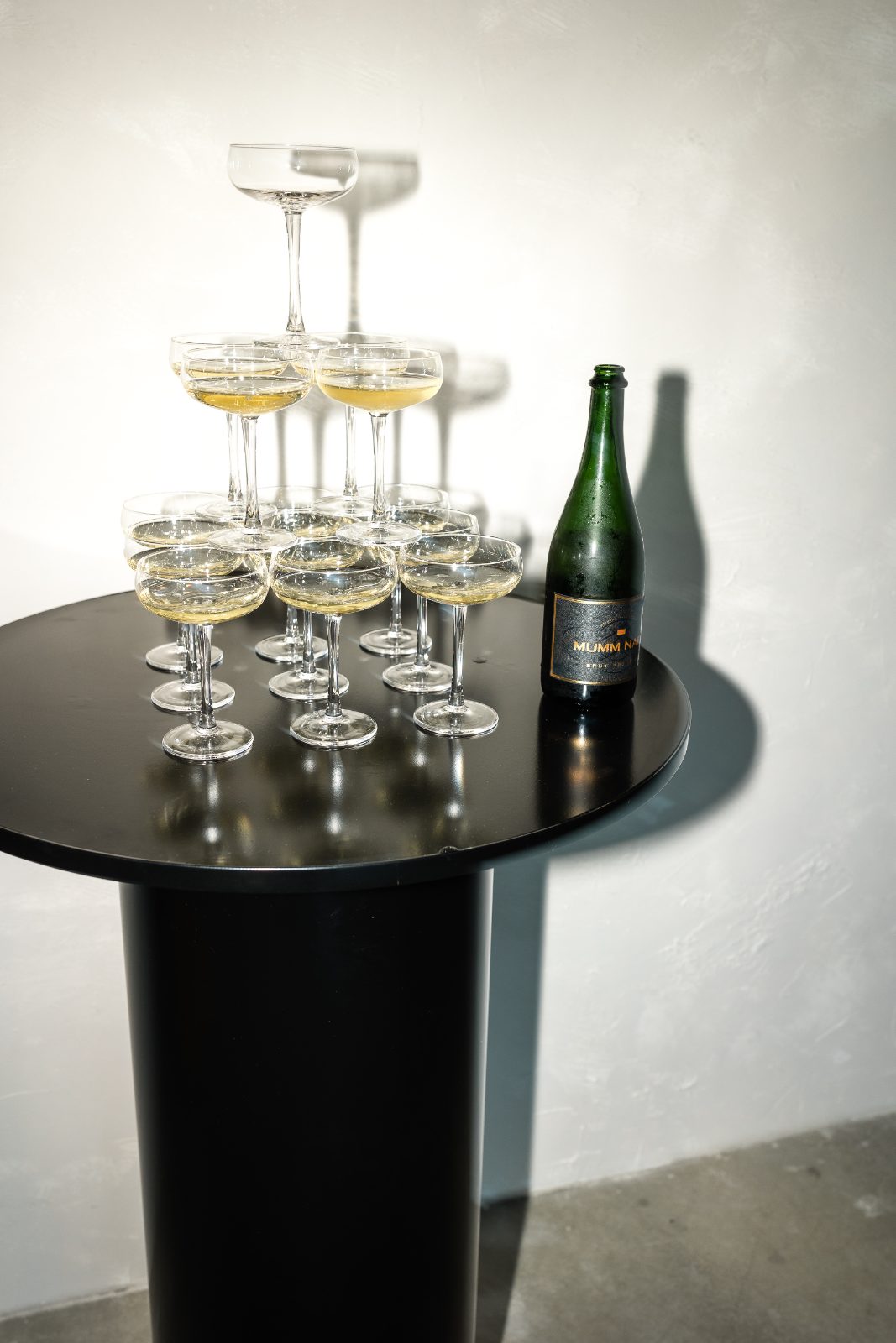 Tower of champagne coupes beside a bottle of sparkling wine on a black cocktail table