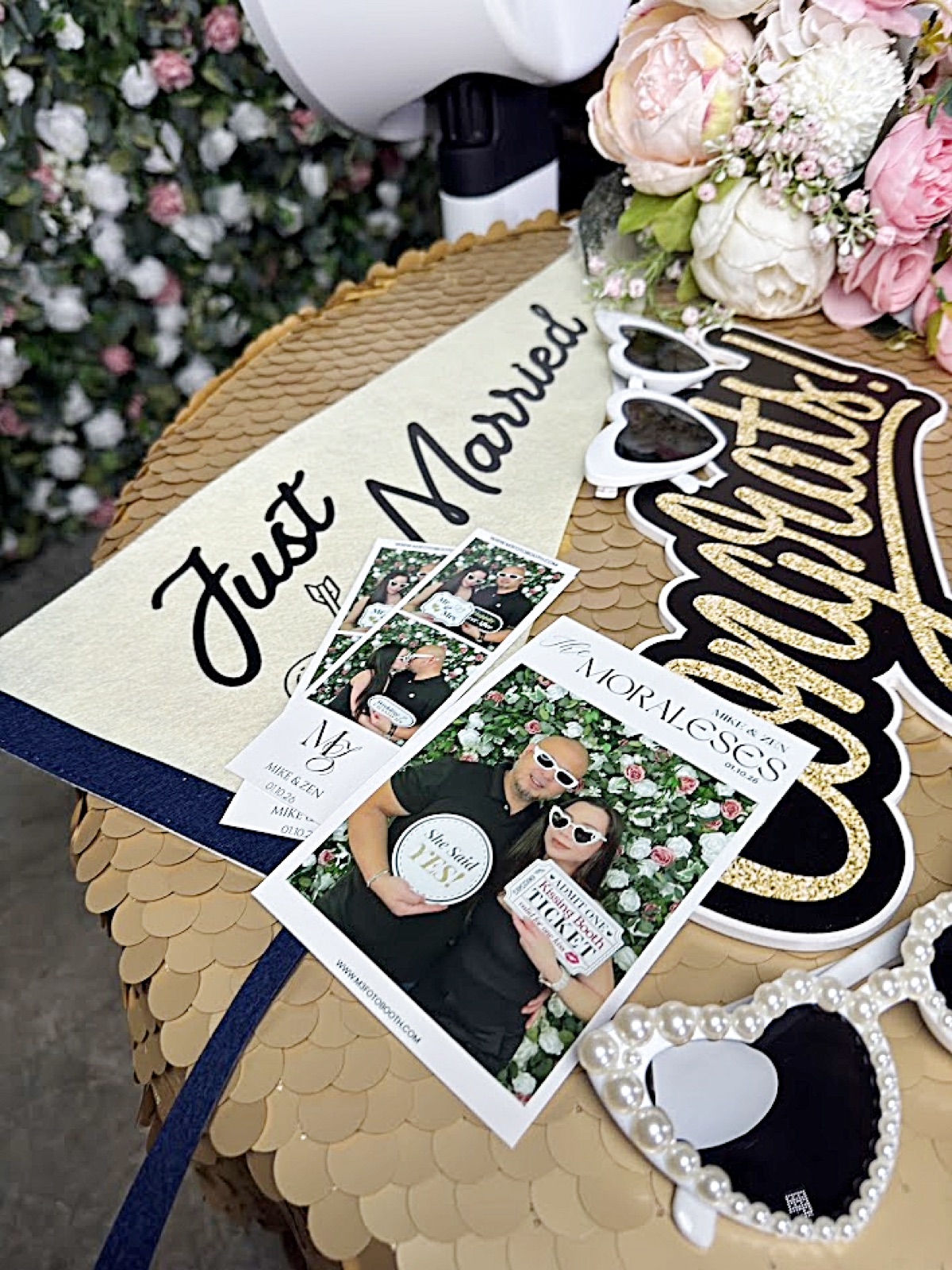 Photo booth prints beside Just Married and Congrats signs and heart sunglasses on a gold sequin table