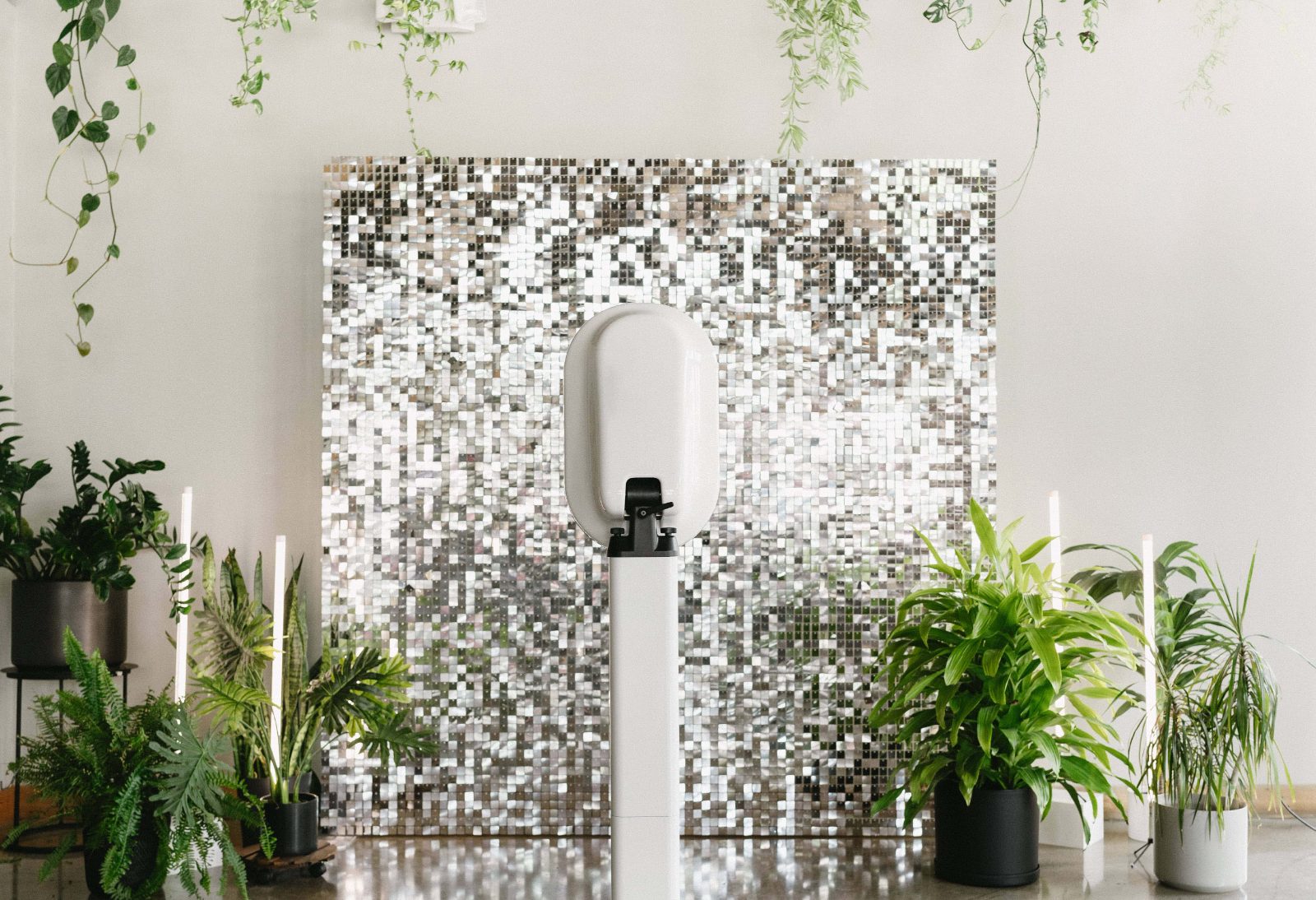 The booth in front of a silver sequin backdrop framed by potted palms, candles and trailing greenery