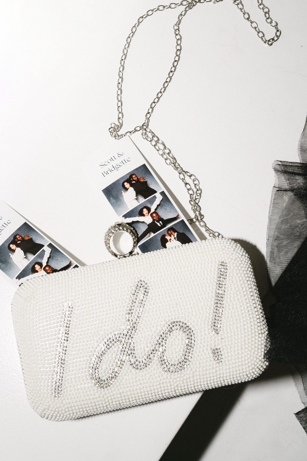 White beaded clutch spelling I do! in rhinestones atop photo booth strips of a couple