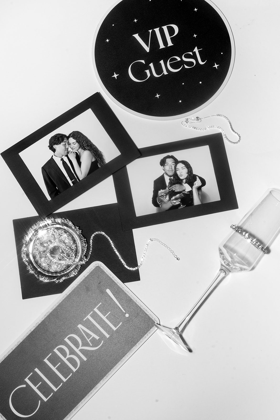 A flat lay of framed black and white photo strips with a VIP Guest badge, a Celebrate sign and a champagne flute